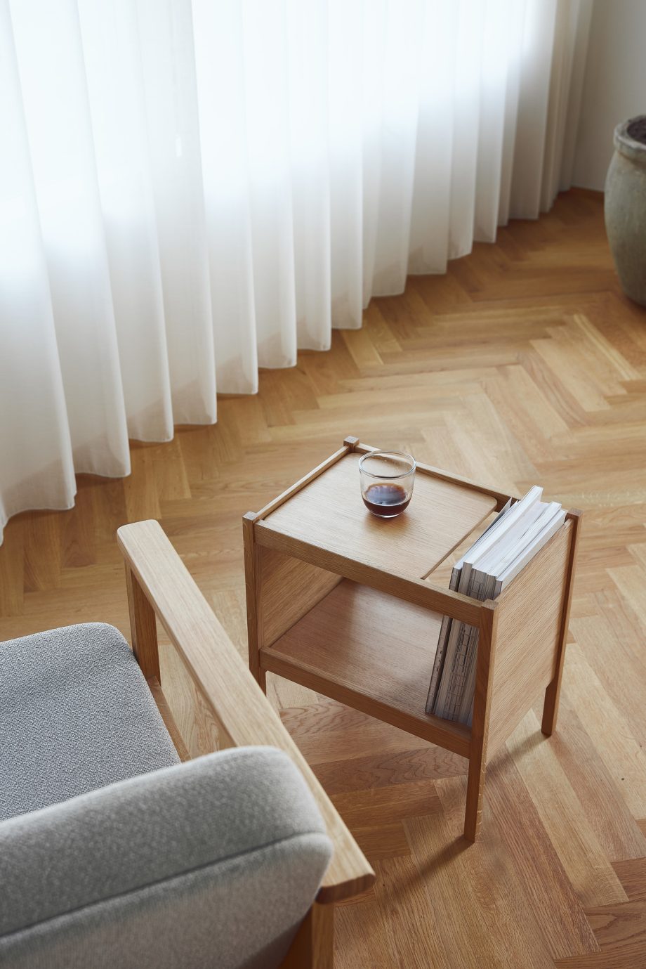 Form Refine Journal bijzettafel in eikenhout als nachttafel naast het bed met tijdschrift, kaars en een minimalistische lamp aan de muur voor een strakke, moderne uitstraling in de slaapkamer.