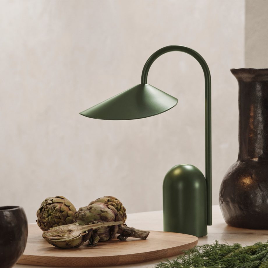 De Ferm Living Arum Portable Lamp in groene uitvoering, geplaatst op een tafel naast artisjokken en een rustiek servies