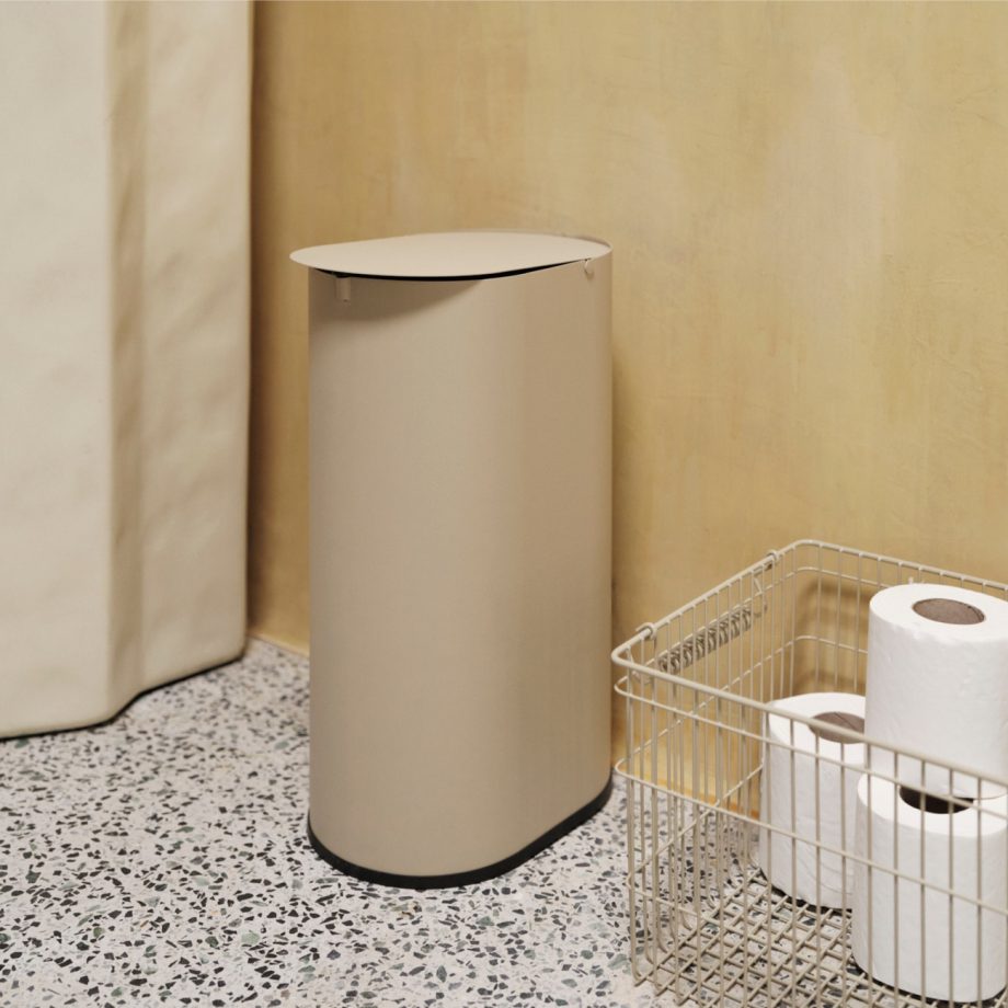 Ferm Living Cala draadmand met toiletrollen en sculpturale pedaalemmer in beige, geplaatst in een moderne badkamer met terrazzo vloer.