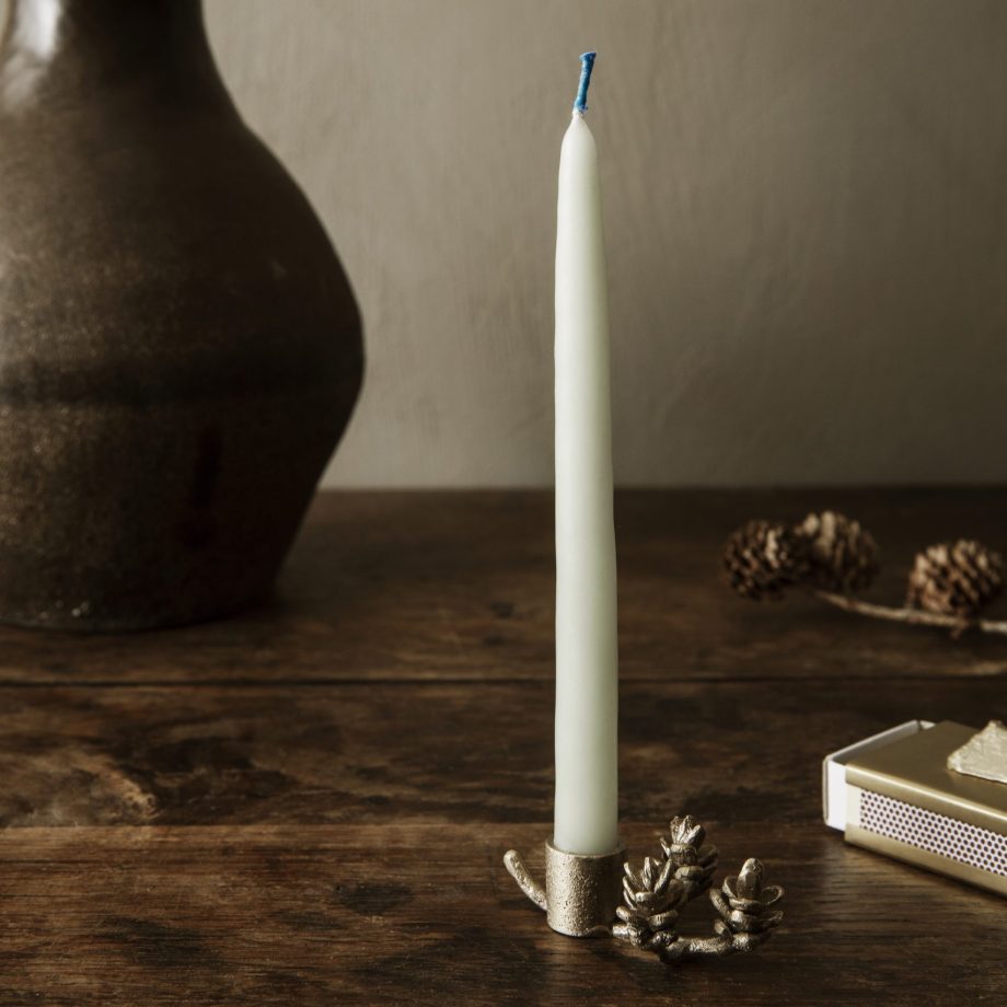 Forest Candle Holder van ferm LIVING in massief messing, afgebeeld op een rustieke houten tafel met een kaars, naast decoratieve elementen zoals een vaas en dennenappels