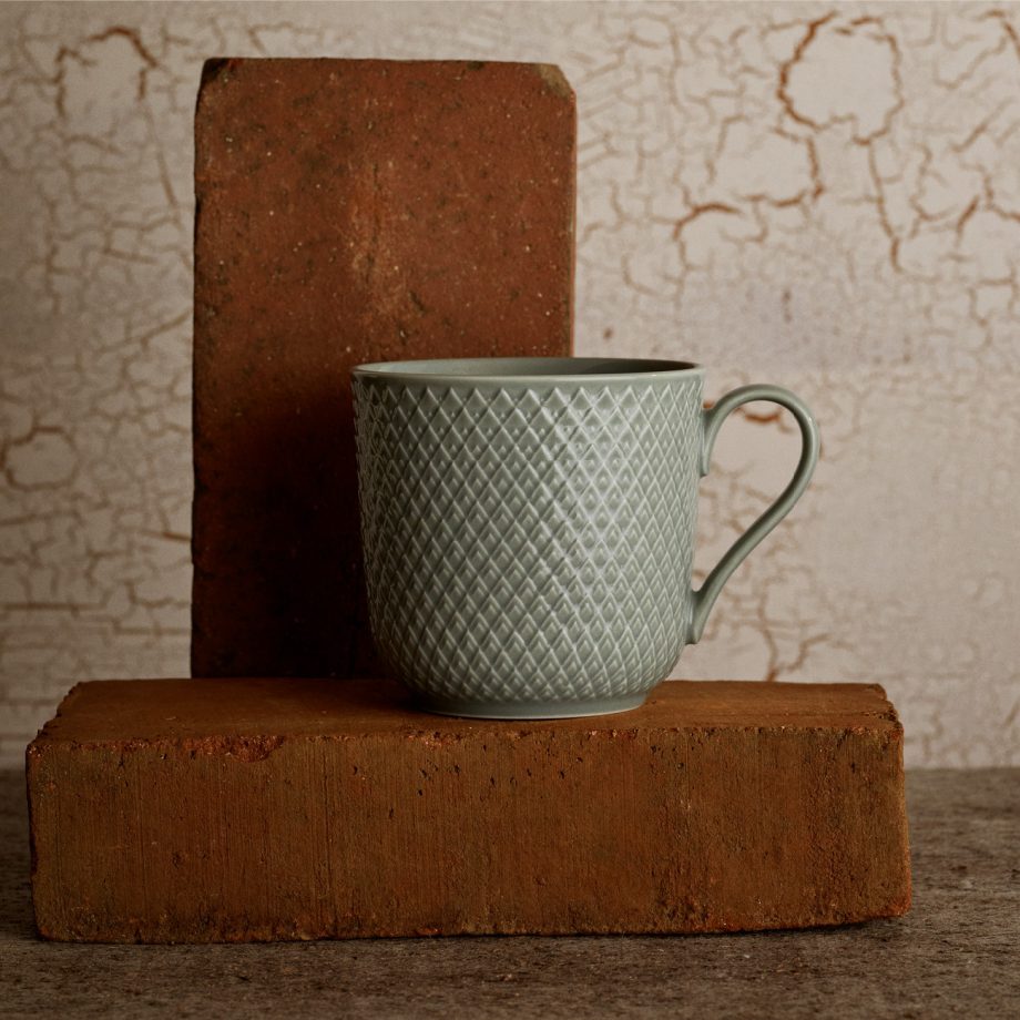 Lyngby Rhombe mok in een zachte vergrijsd groen kleurige aardetint. Luxe porseleinen koffiemok met subtiele reliëfstructuur, perfect voor koffie of thee. Scandinavisch design servies.