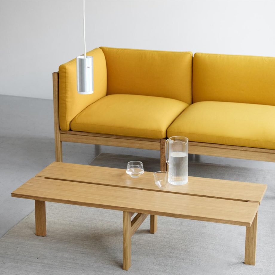 Stijlvolle MOEBE Modular Sofa in warme gele tint, gecombineerd met een minimalistische rechthoekige salontafel van eikenhout. Perfect voor een Scandinavisch interieur met een tijdloze, duurzame uitstraling. Ideaal voor moderne woonkamers en designliefhebbers.