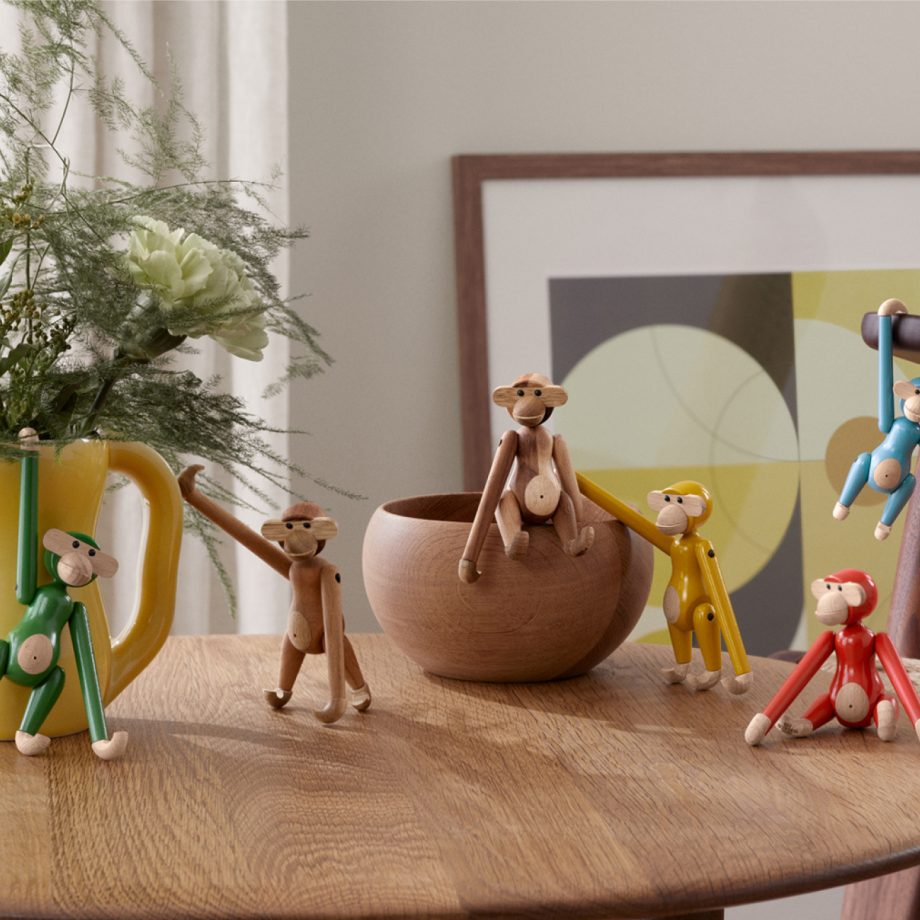 Een speelse collectie van Kay Bojesen Mini Monkey houten aapjes in diverse kleuren, casual gepositioneerd op een houten tafel. De iconische Deense designklassiekers, uitgevoerd in zowel naturel hout als levendige tinten zoals groen, rood, geel en blauw, voegen een speels accent toe aan elk interieur.