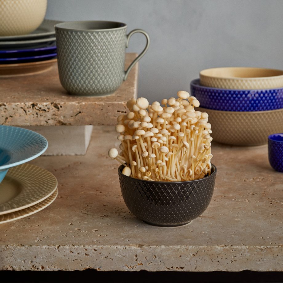 Elegante Lyngby Rhombe schaal van 11 cm in antraciet zwart, gevuld met verse enoki-paddenstoelen. Gemaakt van hoogwaardig porselein met een verfijnd reliëfpatroon. Perfect voor stijlvolle tafelsettings en het serveren van kleine gerechten, snacks of desserts.