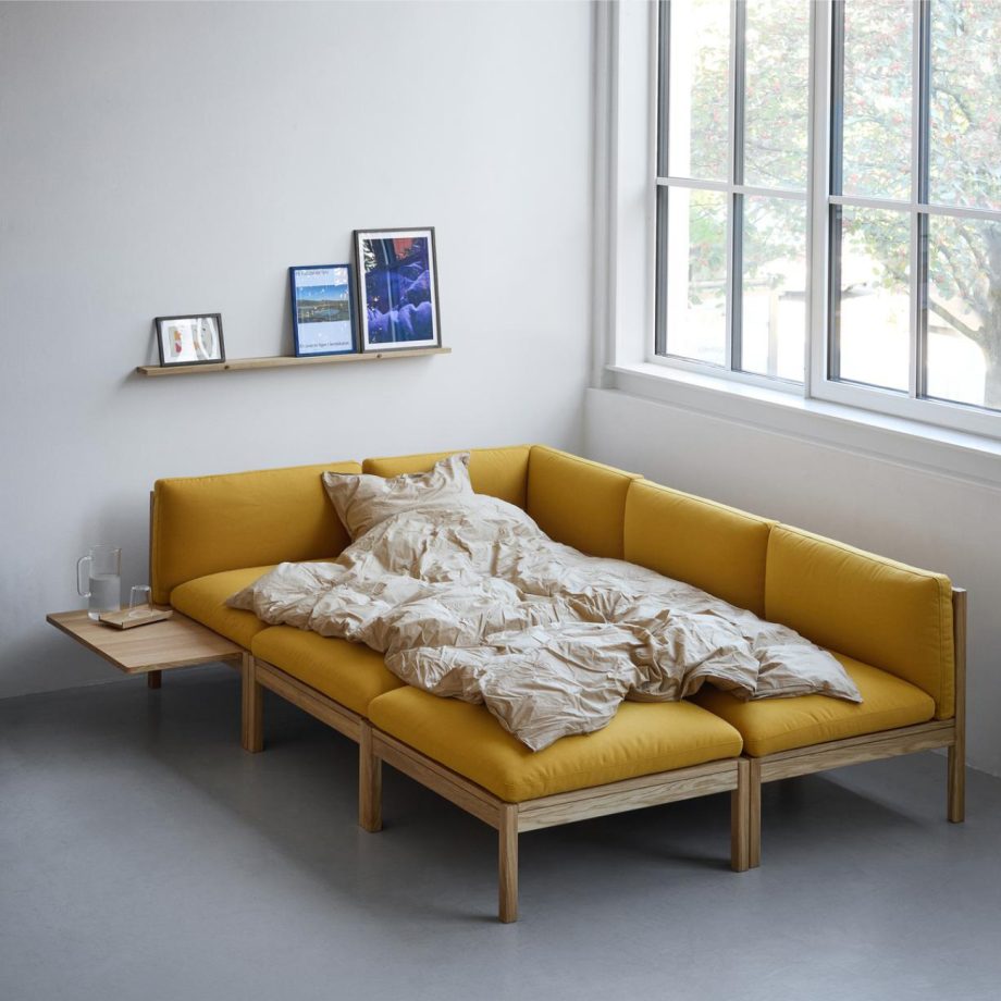 De Moebe Modular Sofa in een warme gele stoffering, flexibel ingericht als loungebank en logeerbed. Dit modulaire zitmeubel combineert Scandinavisch design, duurzaam eikenhout, en aanpasbare modules voor een stijlvolle en veelzijdige woonruimte.