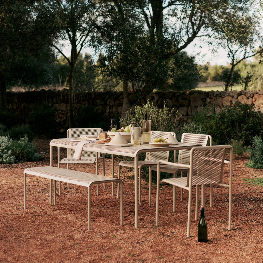 Ferm Living Dapple tuinset in Cashmere, bestaande uit een tafel, bank en stoelen van gegalvaniseerd staal met geperforeerd design, geplaatst op een houten vlonder aan het water voor een serene en stijlvolle buitenbeleving