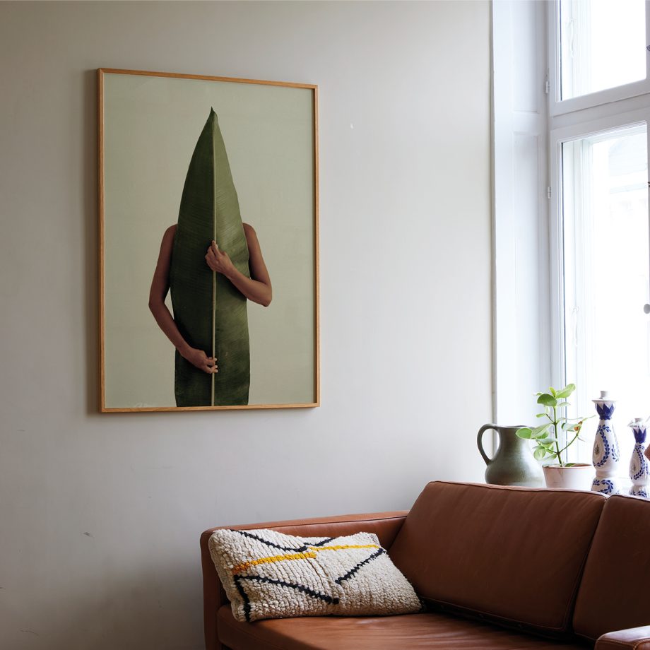 Paper Collective Naturaleza poster foto van figuur achter een grote blad boven bank in woonkamer