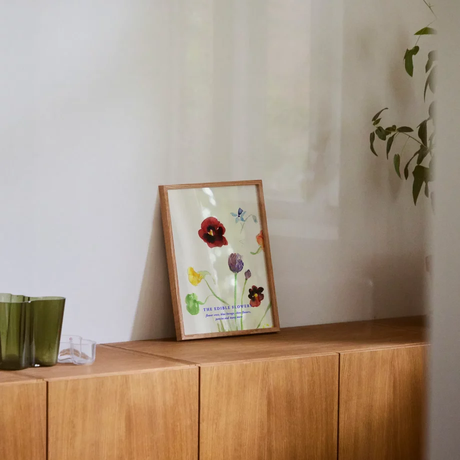 The Edible Flowers poster met kleurrijke bloemen in een eikenhouten 30x40 lijst van Paper Collective op een houten dressuur